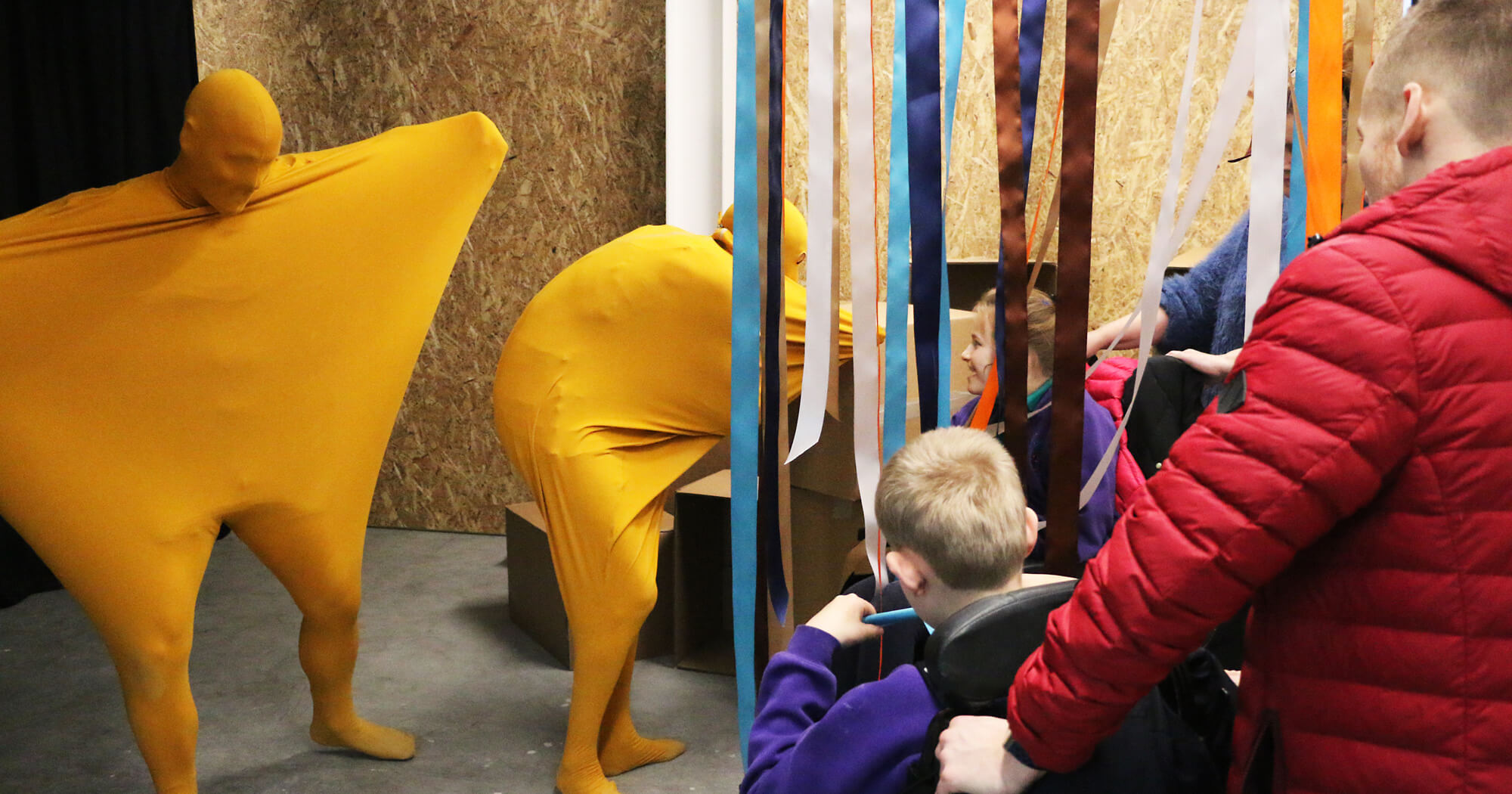 A performance for chidren with PMLD, showing actors wearing stretchy yellow suits interacting with chidren and their carers.