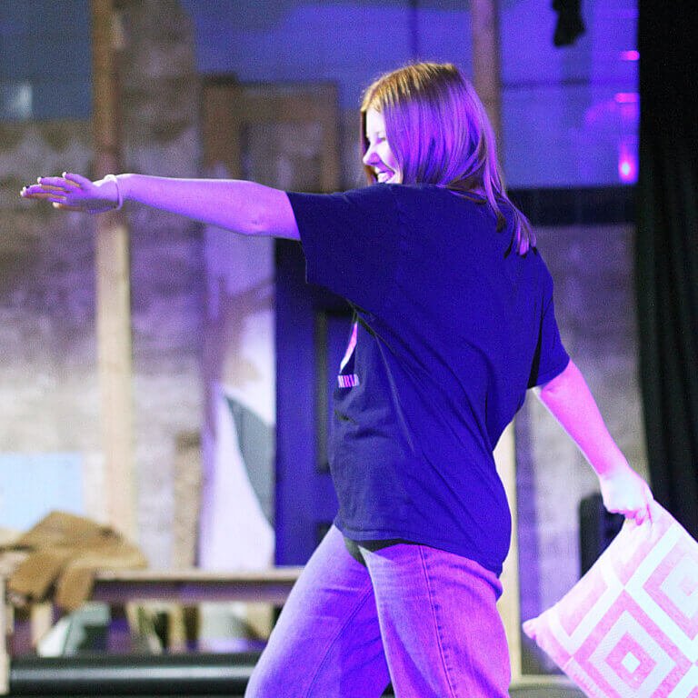 A teenage girl dancing with a cushion in a theatre workshop.